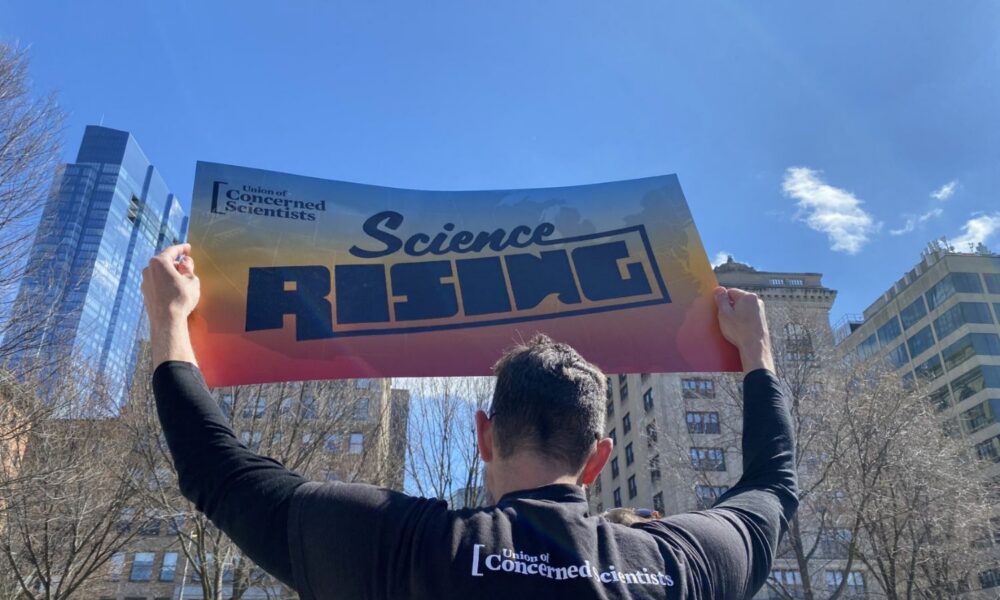 A man holds up a sign reading SCIENCE RISING
