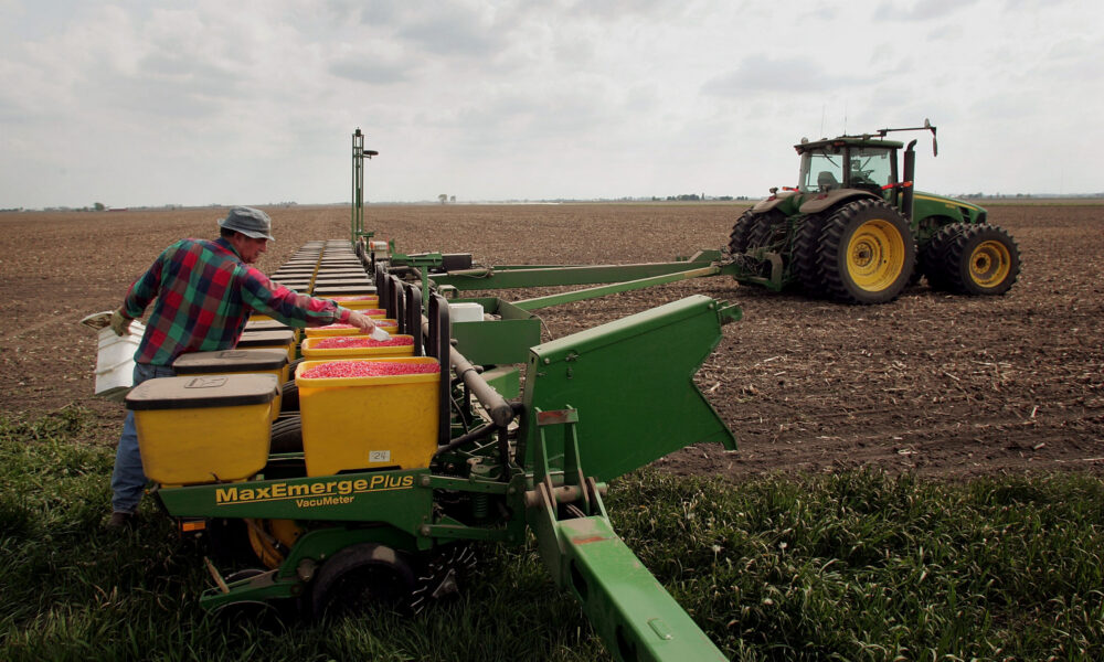 photo of a farmer loading seed corn into the hoppers on a trailer connected to a tractor in the middle of a field