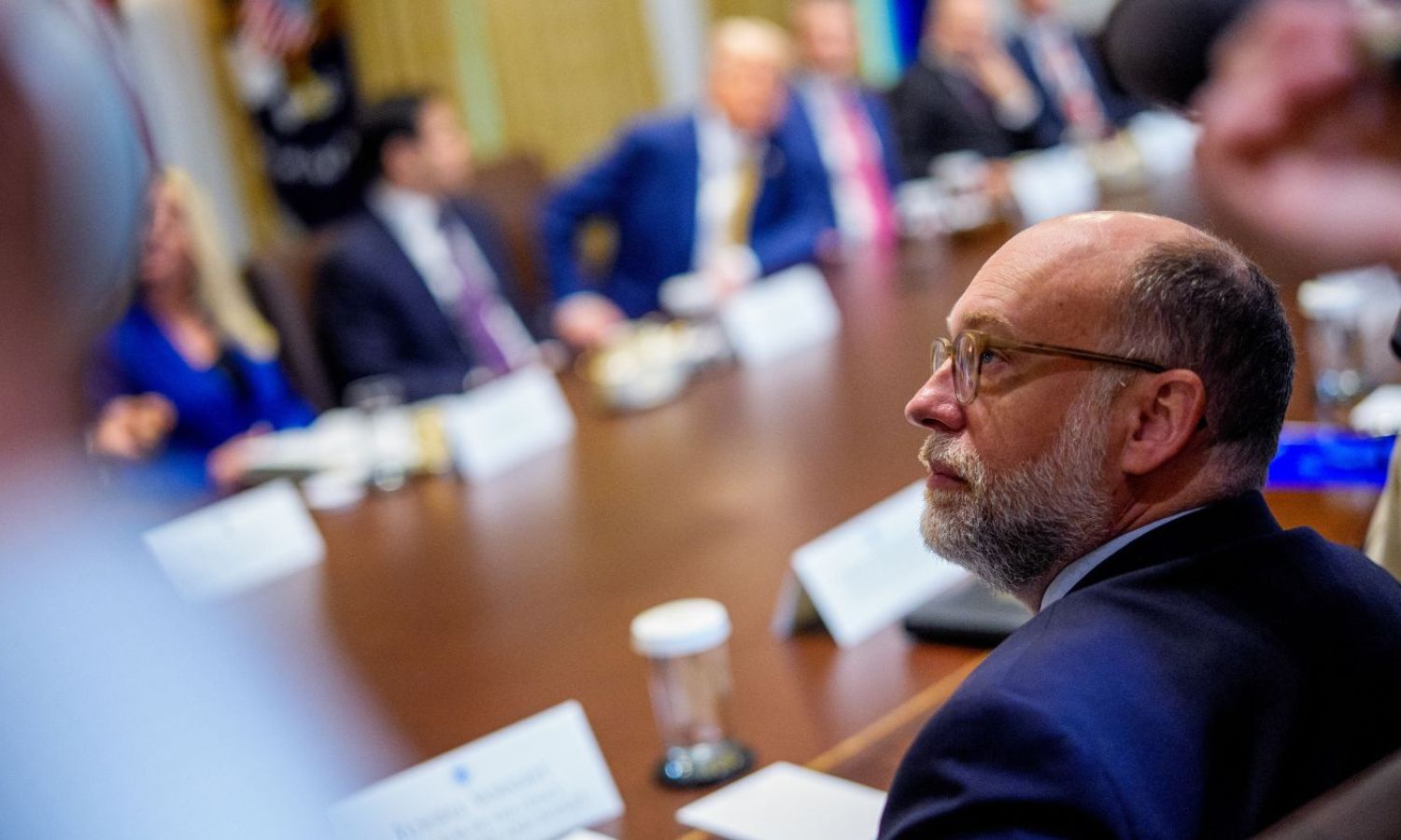 Office of Management and Budget Director Russell Vought is pictured seated at a cabinet meeting in 2025. He appears to be looking at an amorphous blob in the corner of the image.
