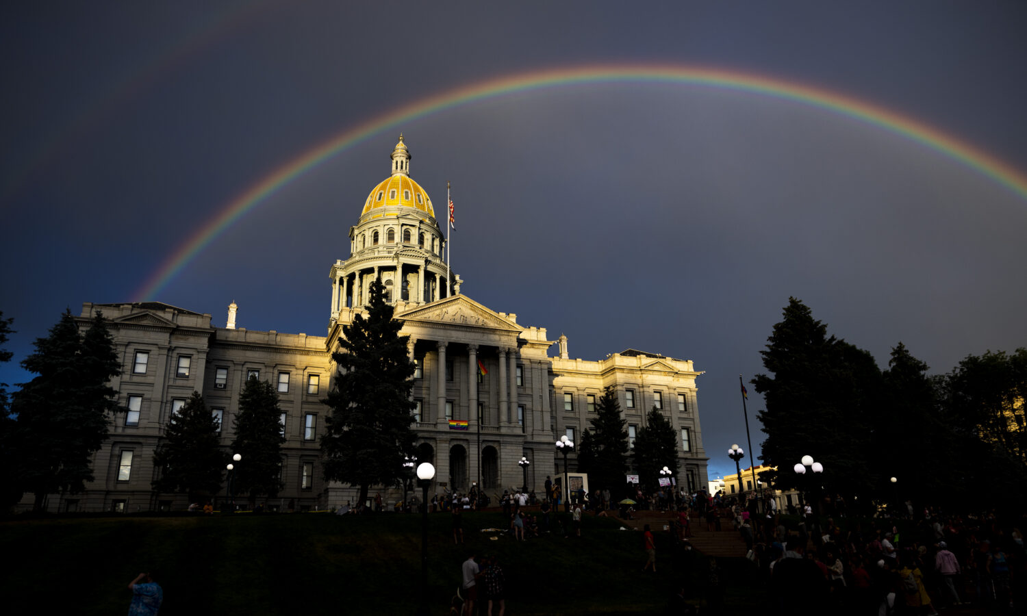 photo of the Colorado state capitol lit by the setting sun; a rainbow arcs across the dark sky above the building