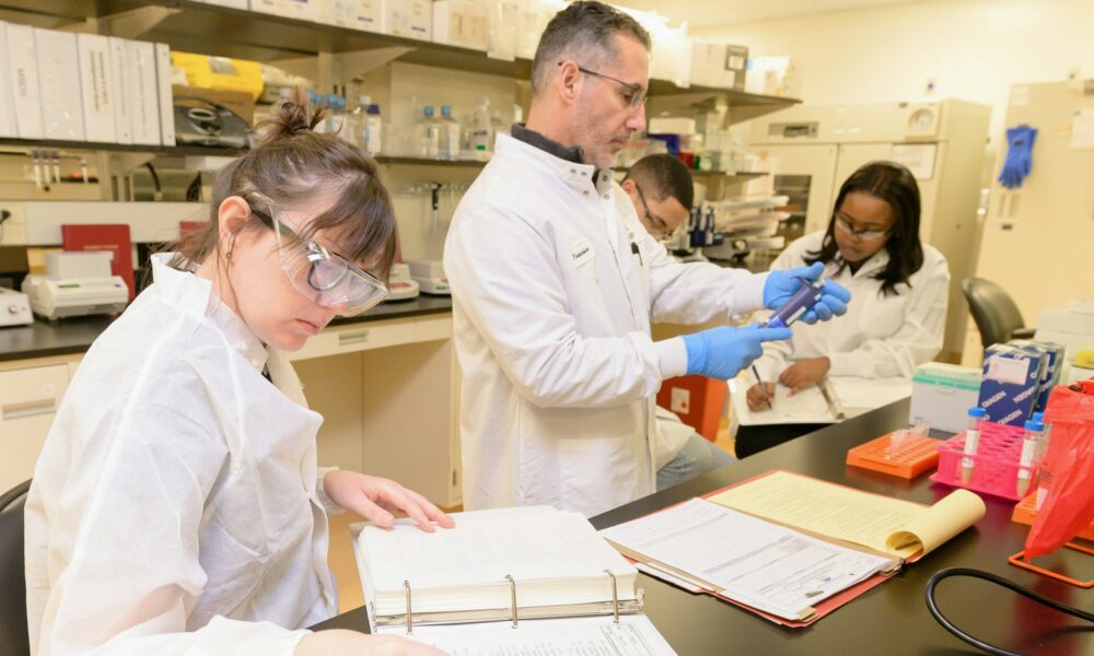 four people in lab coats and goggles carrying out scientific work in a lab