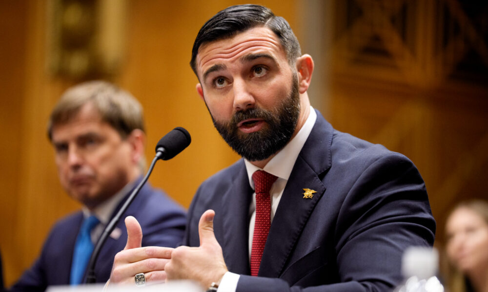 photo of Cameron Hamilton sitting at a microphone and speaking during a Senate committee hearing; the members of the committee are not visible