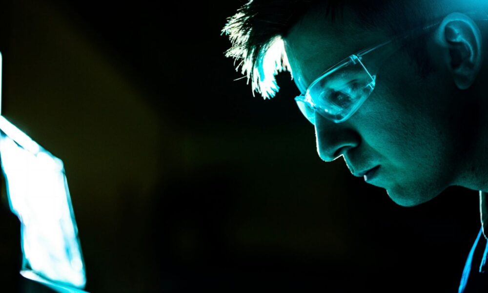 Man wearing glasses looks down at open laptop with blue screen.